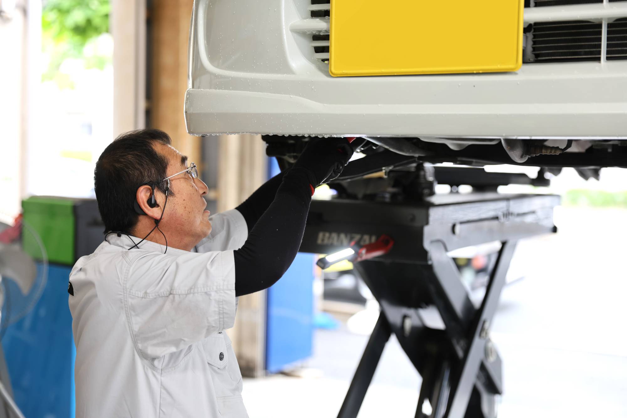 リフトアップされた車の下で作業する白衣の自動車整備士
