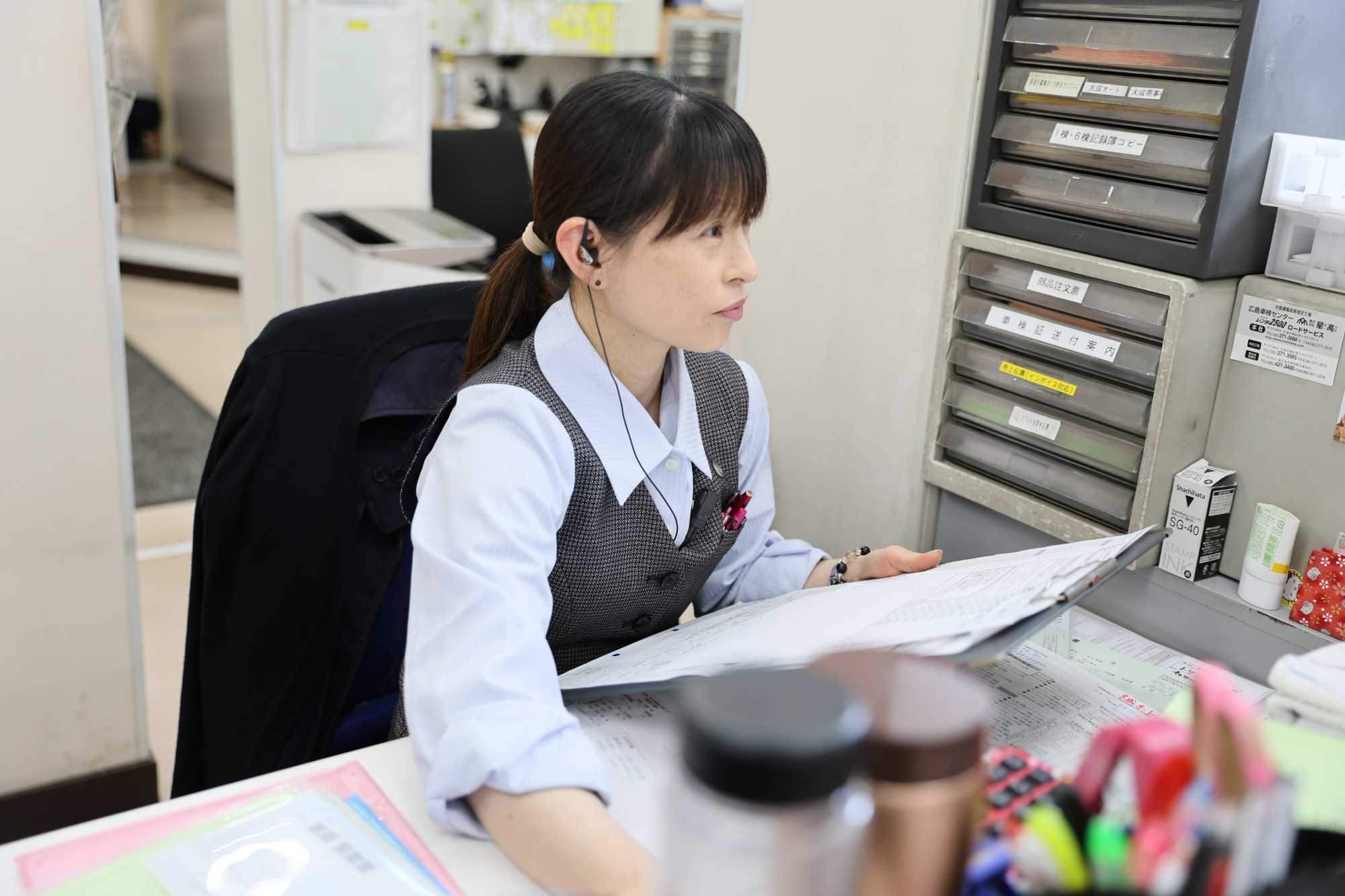 オフィスでヘッドセットをつけて書類を確認する女性事務員