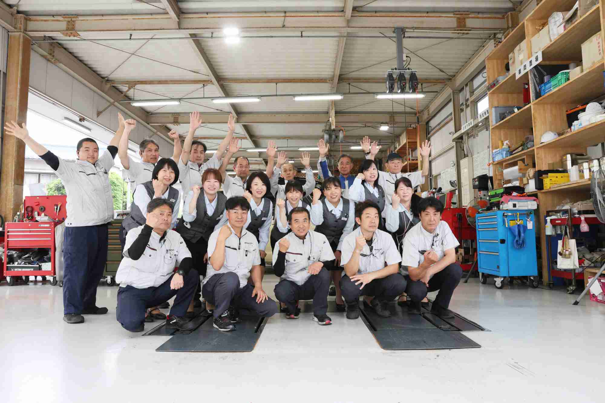 整備服を着た男女スタッフが工場で笑顔でポーズを取る様子