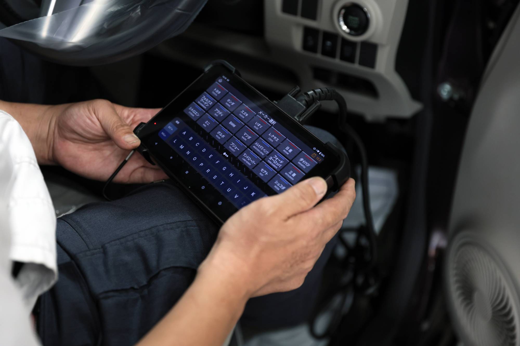 車内で自動車故障診断機を操作する技術者の手元
