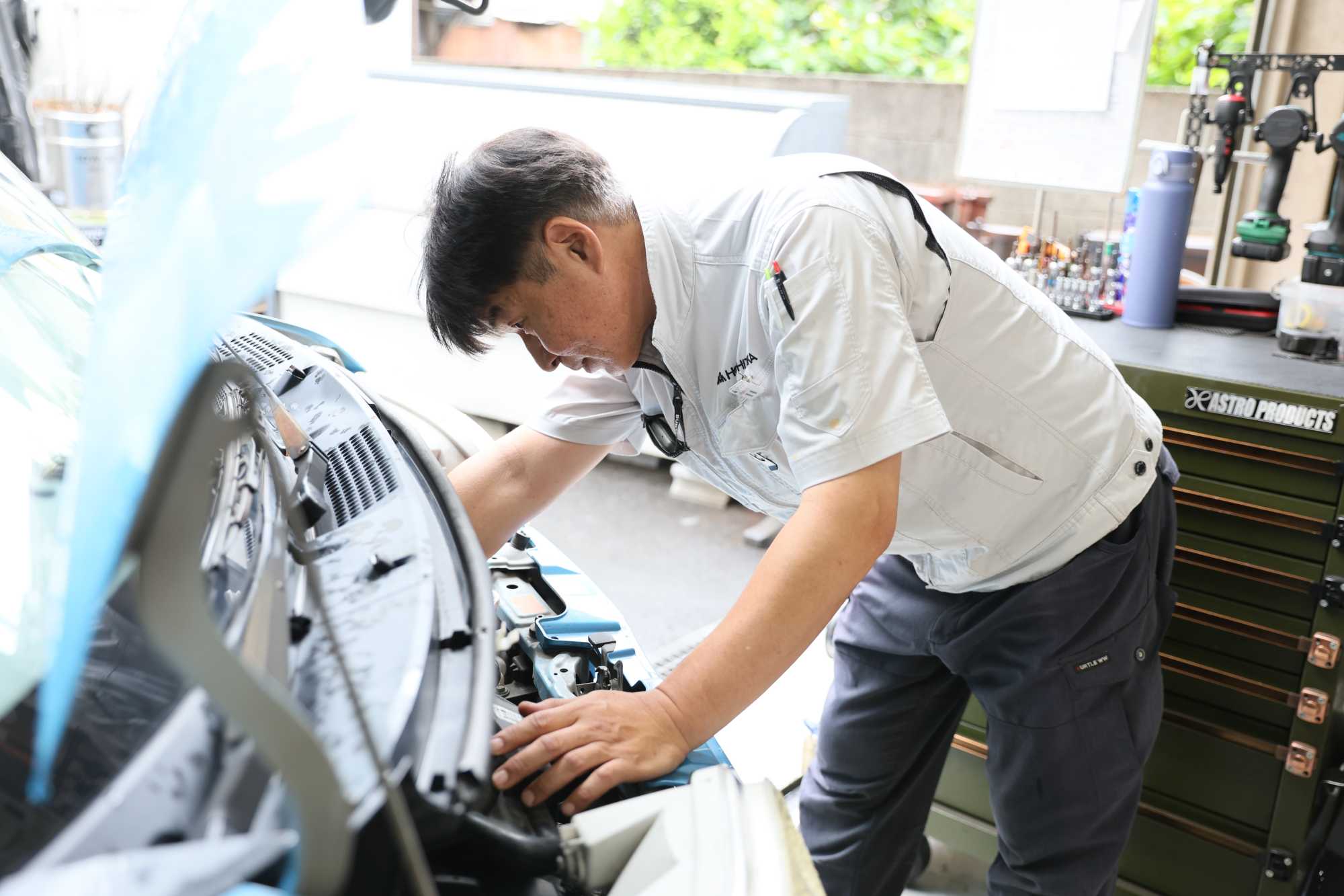 白い作業着を着た男性技術者が自動車エンジン点検作業をしている様子