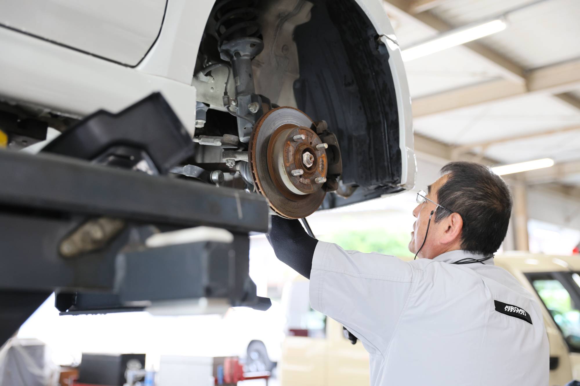 作業着の男性がリフトアップした車両のブレーキを確認する様子