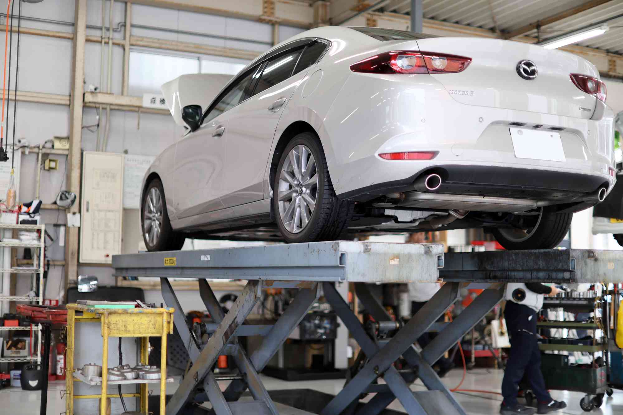 整備工場のリフトで点検中の白いセダン車