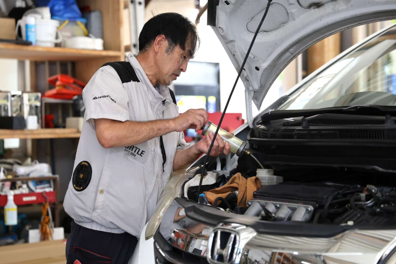 作業服を着た男性がボンネットを開けて車両整備をしている様子