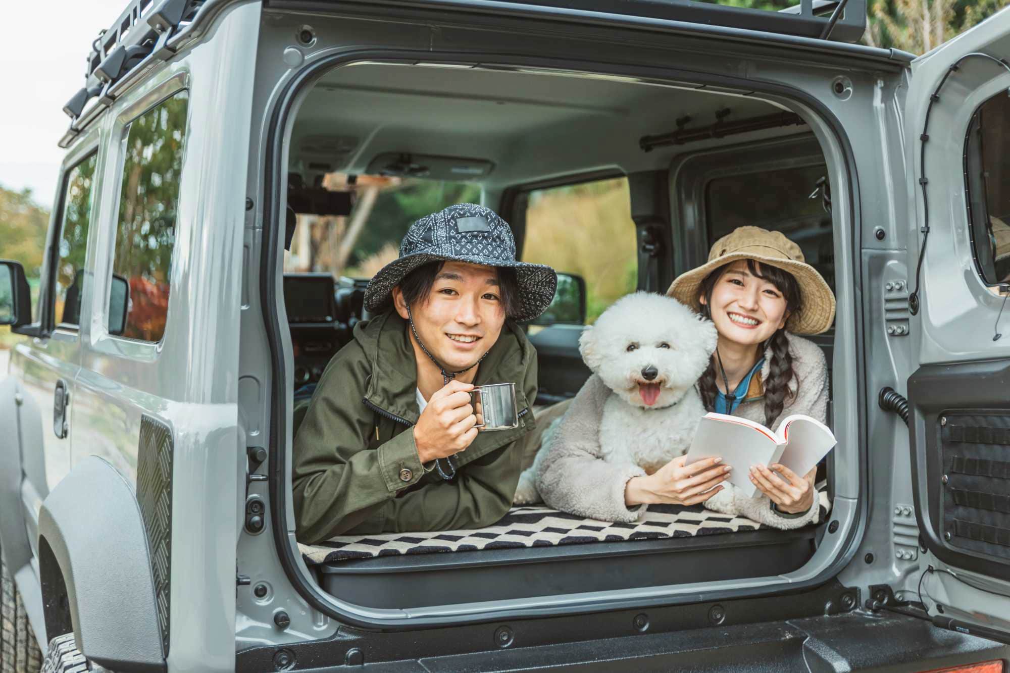 キャンピングカーの荷台にいる若いカップルと白い犬